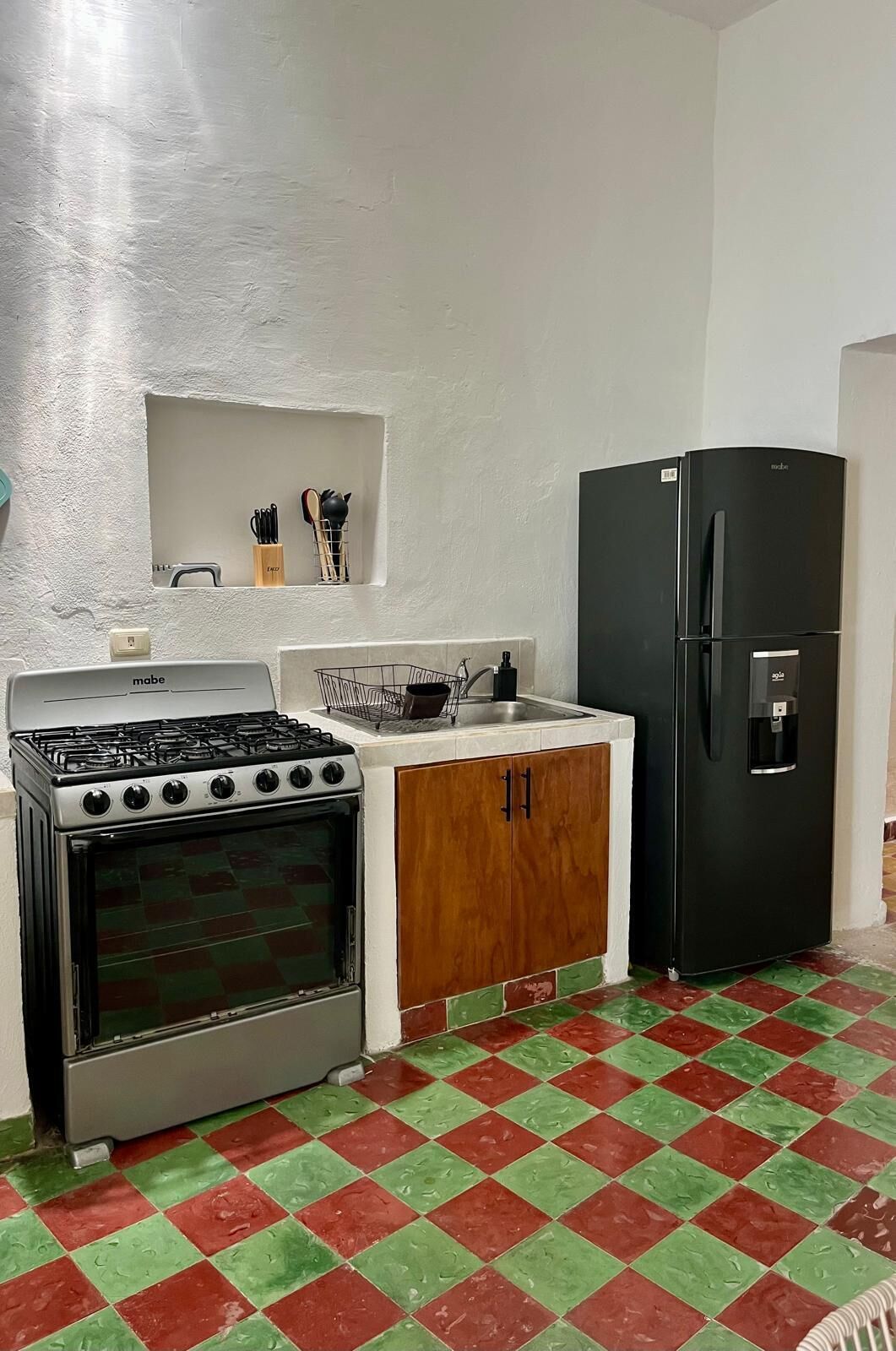 A compact kitchen with a gas stove, a built-in oven, a sink, and a black refrigerator.
