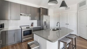 Een moderne keuken met grijze kastjes, roestvrijstalen apparatuur, een centraal eiland met barkrukken en hanglampen.