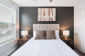 Et hotelværelse med en stor seng, to sengeborde med lamper, en mørk væg og et vindue med persienner.