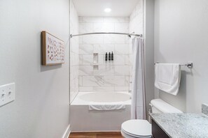 Et badeværelse med bruser, badekar, toilet og et håndklædetørrestativ.
