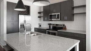 A modern kitchen with dark cabinets, stainless steel appliances, a granite countertop, and pendant lighting.