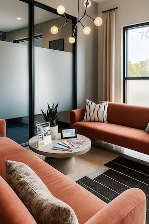 Ein modernes Wohnzimmer mit einer Couch, einem Couchtisch mit Zeitschriften, einer Pflanze und einer Pendelleuchte.
