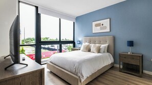 Een slaapkamer met een groot bed, een televisie, een nachtkastje en een raam met uitzicht.