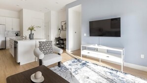 A modern living space with a kitchen, dining area, and a TV mounted on a wall. - Landing | Beautiful 2BD, Pool (Casas Adobes)