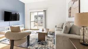 Ein modernes Wohnzimmer mit Flachbildfernseher, einer Couch, einem Couchtisch und einer Glaslampe.