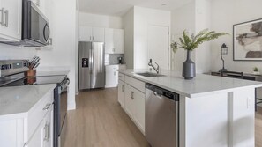 A modern kitchen with stainless steel appliances, white cabinetry, and a central island with a sink. - Landing | Incredible 2BD, Pool (Casas Adobes)