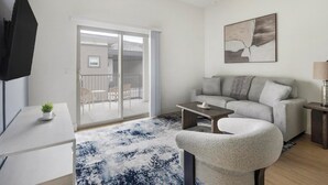 En moderne stue med sofa, sofabord, tv og en skydedør til et udendørs område.