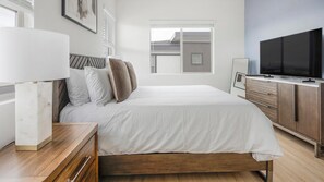 A modern bedroom with a bed, bedside tables, a TV, and a window. - Landing | Incredible 2BD, Pool (Casas Adobes)