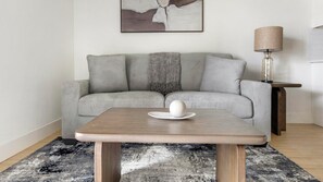 A modern living room with a grey sofa, a wooden coffee table, and a lamp. - Landing | Incredible 2BD, Pool (Casas Adobes)