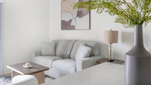 En moderne stue med sofa, sofabord, lampe og en vase med plante.