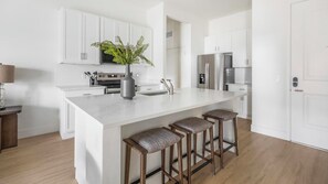 A modern kitchen with white cabinetry, a marble countertop, a central island with bar stools, and stainless steel appliances. - Landing | Incredible 2BD, Pool (Casas Adobes)