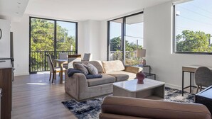 A modern living room with a sofa, coffee table, and a dining area with chairs. - Landing | Beautiful 2BD, Yoga Studio, Game Room (Miami)