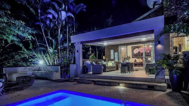 A modern outdoor pool area with a patio, seating, and a well-lit interior space.