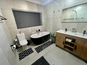 Un baño moderno con inodoro, bidé, bañera, tocador con espejo y estante para toallas.