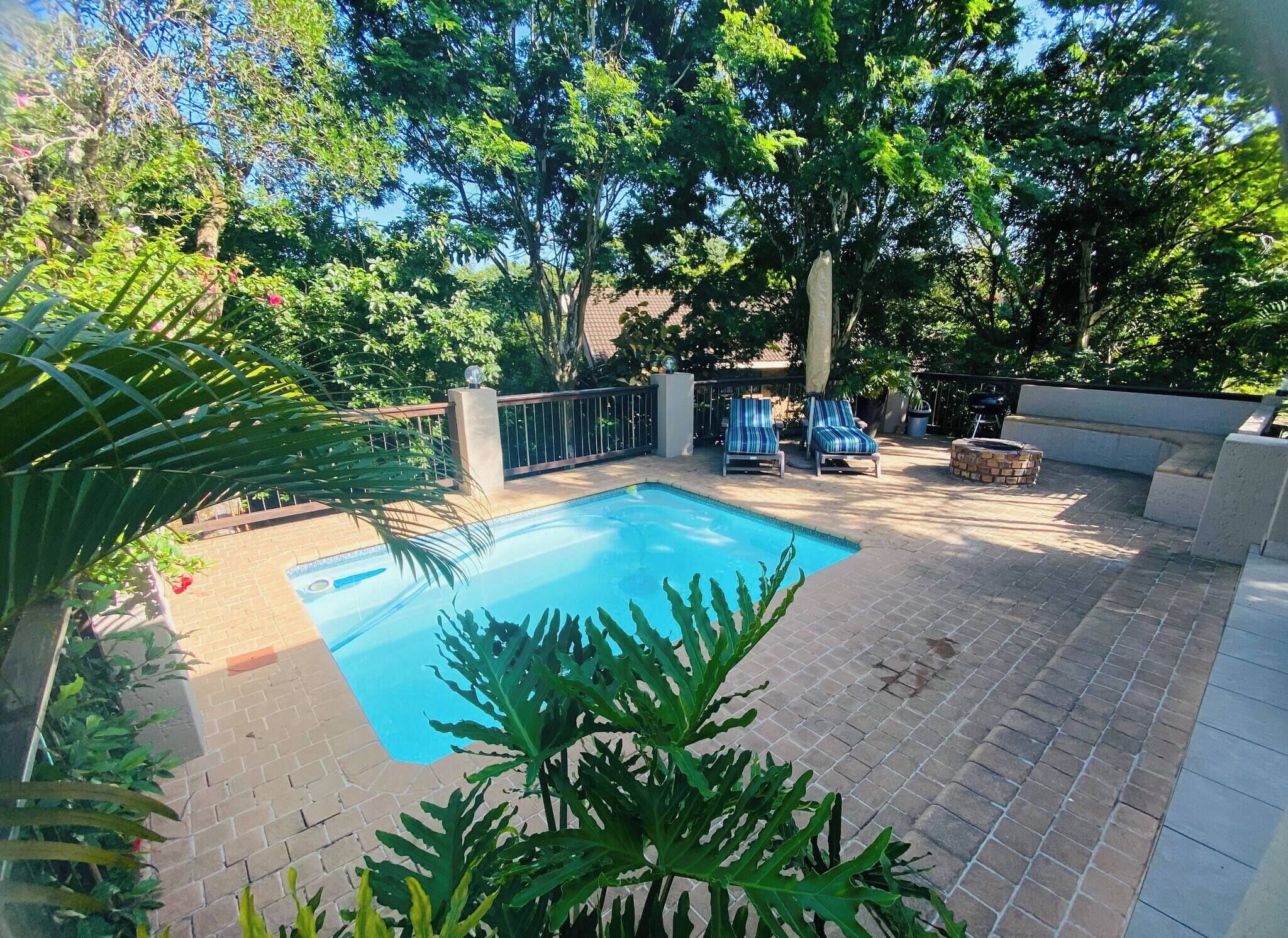 A swimming pool with a tiled deck, surrounded by trees and a fence.