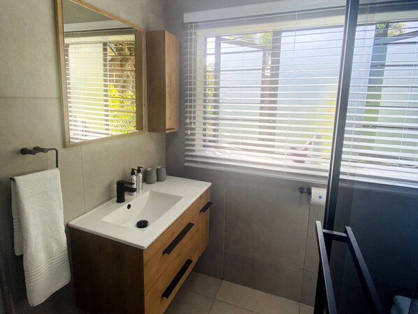 A modern bathroom with a large mirror, a sink, and a window with blinds.