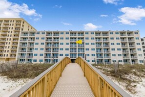 A multi-story hotel with a central staircase leading to the entrance, surrounded by sandy beach and a wooden walkway. - Island Shores 152 (Gulf Shores)