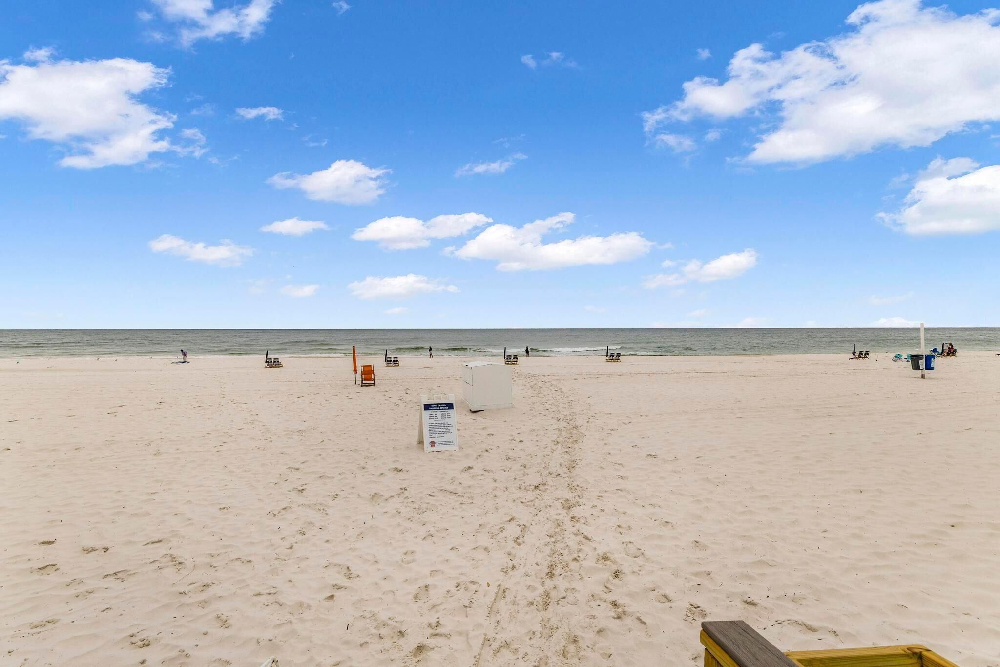 Una extensa playa arenosa con cielo despejado y algunas nubes, una torre de salvavidas y un cartel.