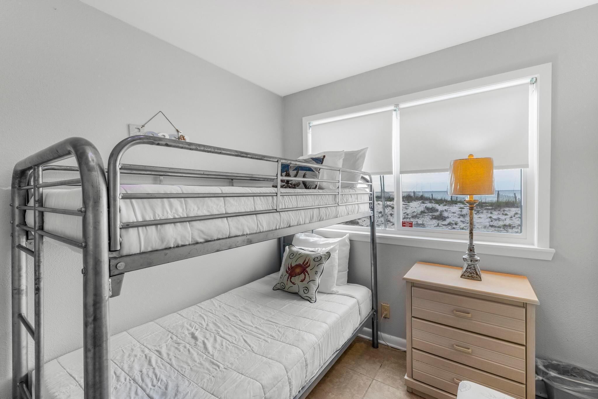 Une chambre avec un lit superposé, une fenêtre, une lampe de chevet et une petite commode.