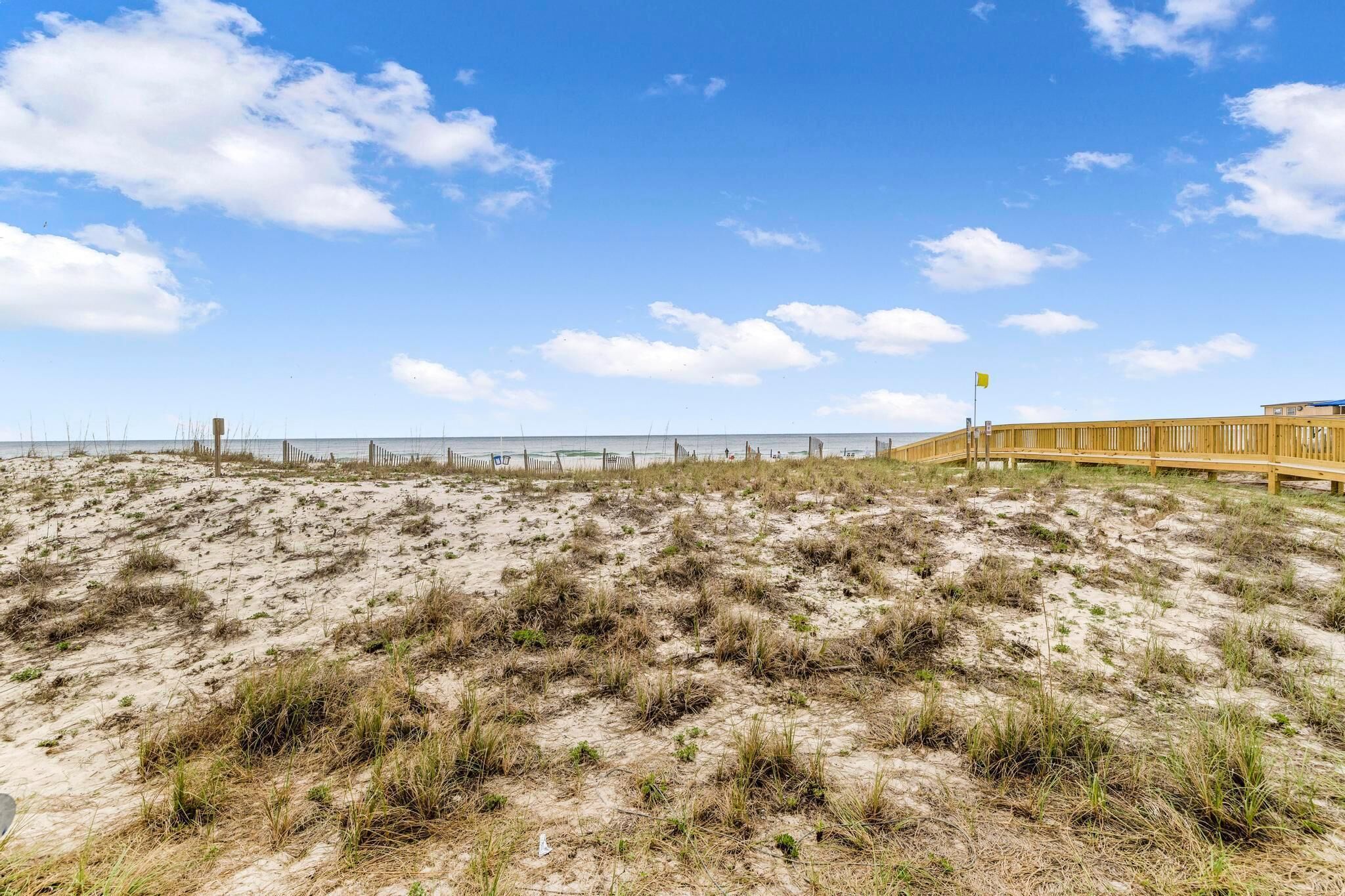 A sandy beach with a wooden fence and a flagpole.