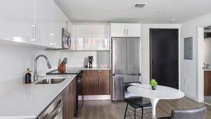 A modern kitchen with stainless steel appliances, a dining area with a round table, and a dark door. - Landing | Chic Studio, Yoga Studio, Game Room (Miami)