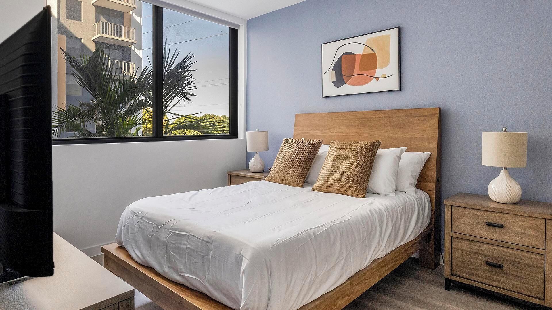 A bedroom with a bed, nightstands, a window, and a wall-mounted picture.