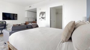 Ein modernes Schlafzimmer mit einem großen Bett, einer Couch, einem Fernseher und einer kleinen Küche im Hintergrund.
