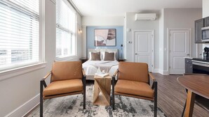 Ein Hotelzimmer mit einem Bett, zwei Sesseln, einem kleinen Tisch, einem Gemälde und einer Küchenzeile.