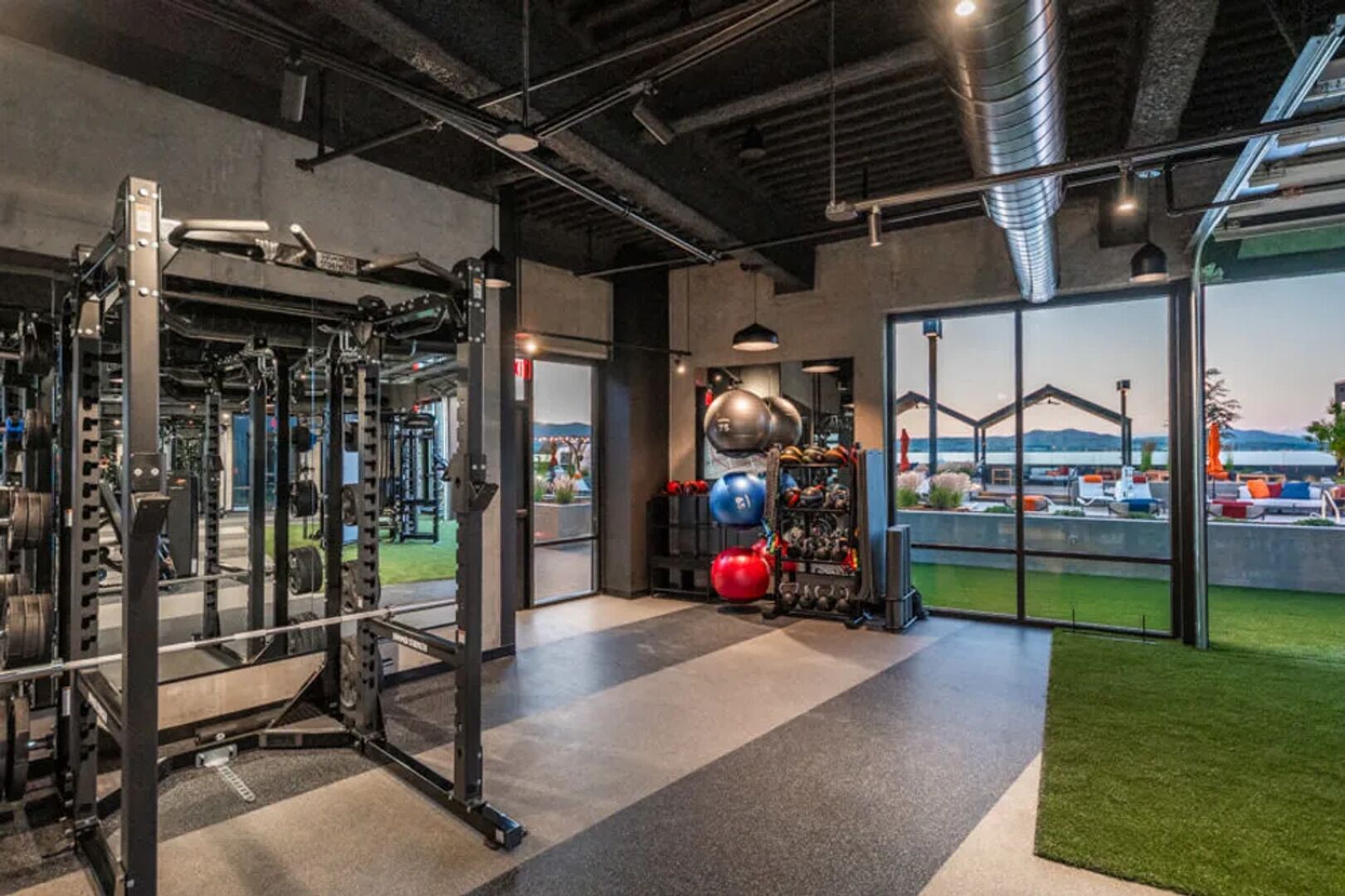 Een fitnessruimte met gewichthefapparatuur, een kettlebellrek en uitzicht op een zwembad en buitengebied.