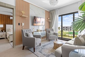 A modern living room with a TV, two armchairs, a sofa, a coffee table, and a view of the outside. - NOK Modern 2BR with Rooftop Jacuzzi By Vistacana (Punta Cana)