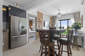A modern kitchen with a stainless steel refrigerator, wooden chairs, a dining table, and a large window. - NOK Modern 2BR with Rooftop Jacuzzi By Vistacana (Punta Cana)