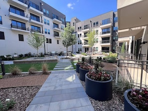 A courtyard with a pathway, outdoor seating, and planters. - Landing | Chic 1BD, Clubhouse (Tulsa)