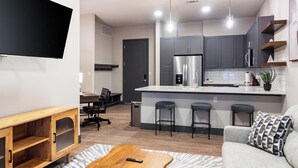 Ein modernes Wohnzimmer mit Couchtisch aus Holz, einer grauen Couch und einer Küche mit grauen Schränken und Edelstahlgeräten.