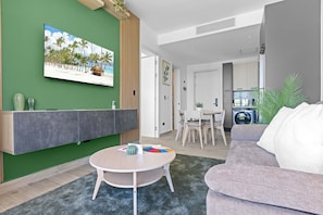 A modern living room with a green accent wall, a round table, a grey sofa, and a painting of a beach scene. - NOK Stylish 1BR Apartment  the Towers by Vistacana (Punta Cana)