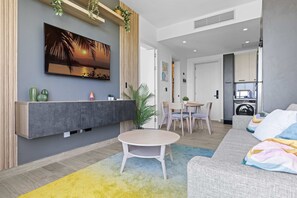 A modern living room with a flat-screen TV, a sofa, a round table, and a dining area. - NOK Elegant 1BR The Towers by Vistacana (Punta Cana)