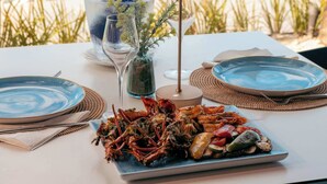Una mesa con una bandeja de mariscos, un vaso de agua, una botella de champán y vistas a un lago con palmeras.