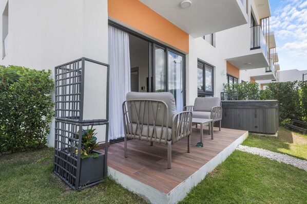 A modern outdoor patio with a wooden deck, two chairs, a potted plant, and a hot tub. - NOK Modern 1BR  with Terrace by Vistacana rentals (Punta Cana)