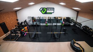 Ein Fitnessraum mit Trainingsgeräten, einer Spiegelwand und einem Logo an der Decke.