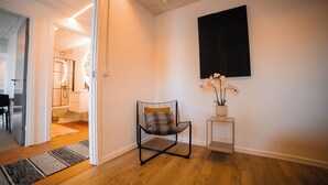 Ein modernes Interieur mit freiem Blick auf einen Flur, der zu einem Badezimmer führt, ein schwarzer Sessel mit Kissen und eine Orchidee im Topf auf einem kleinen Tisch.