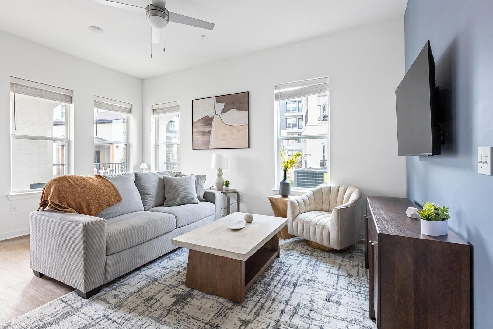 Ein modernes Wohnzimmer mit Sofa, Sessel, Couchtisch und einem wandmontierten Flachbildfernseher.