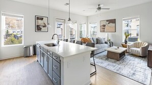 Una cocina moderna con una isla central, un área de comedor con mesa y sillas, un sofá y un ventilador de techo.