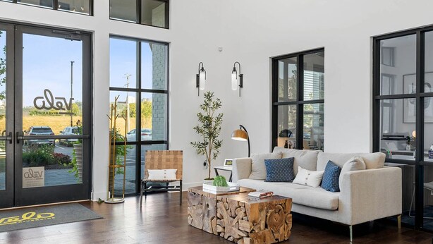 Una sala de estar moderna con sofá, mesa de centro y sillón. Amplias ventanas ofrecen vistas al exterior.