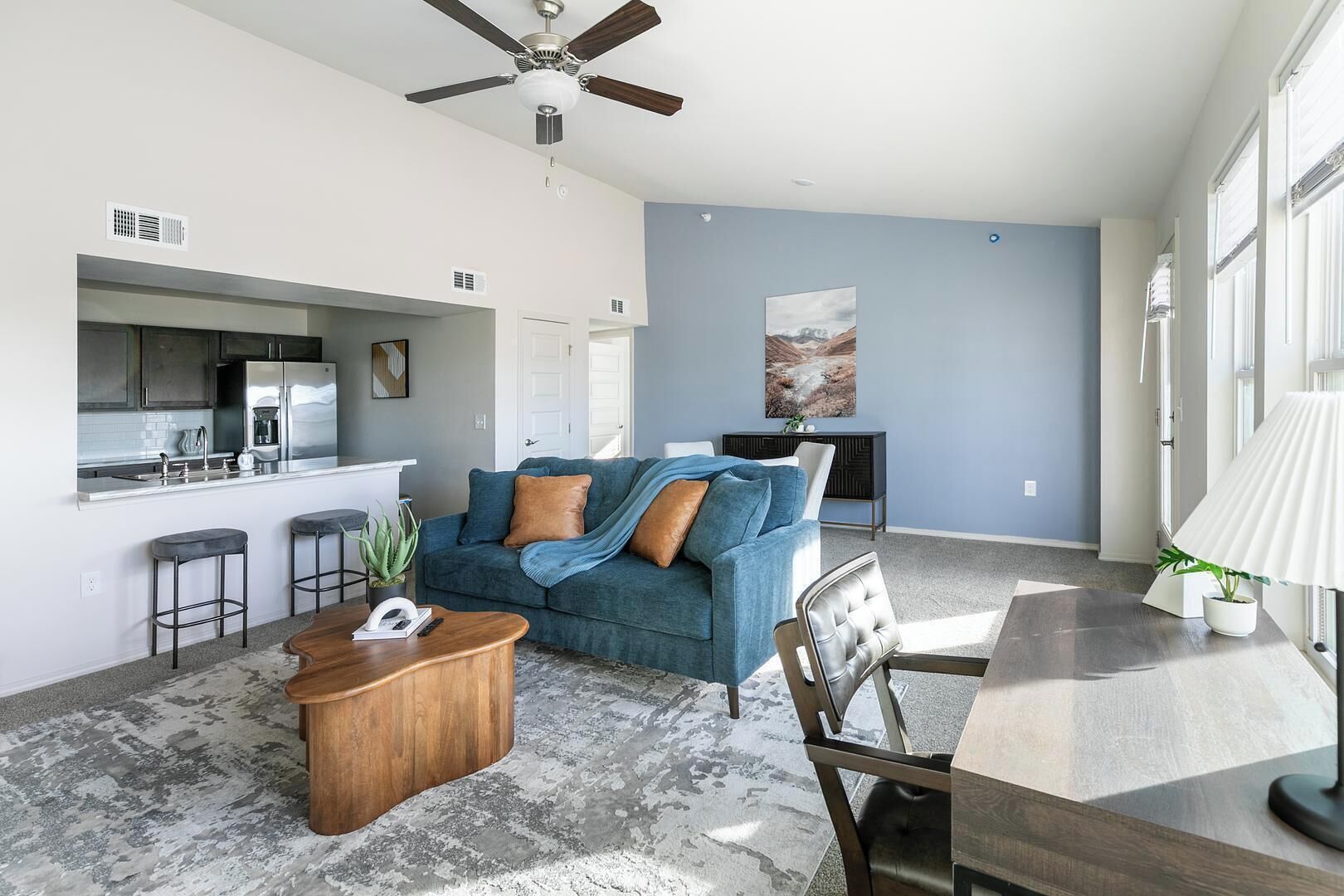 A modern living room with a blue sofa, wooden coffee table, and a dining area with a lamp.