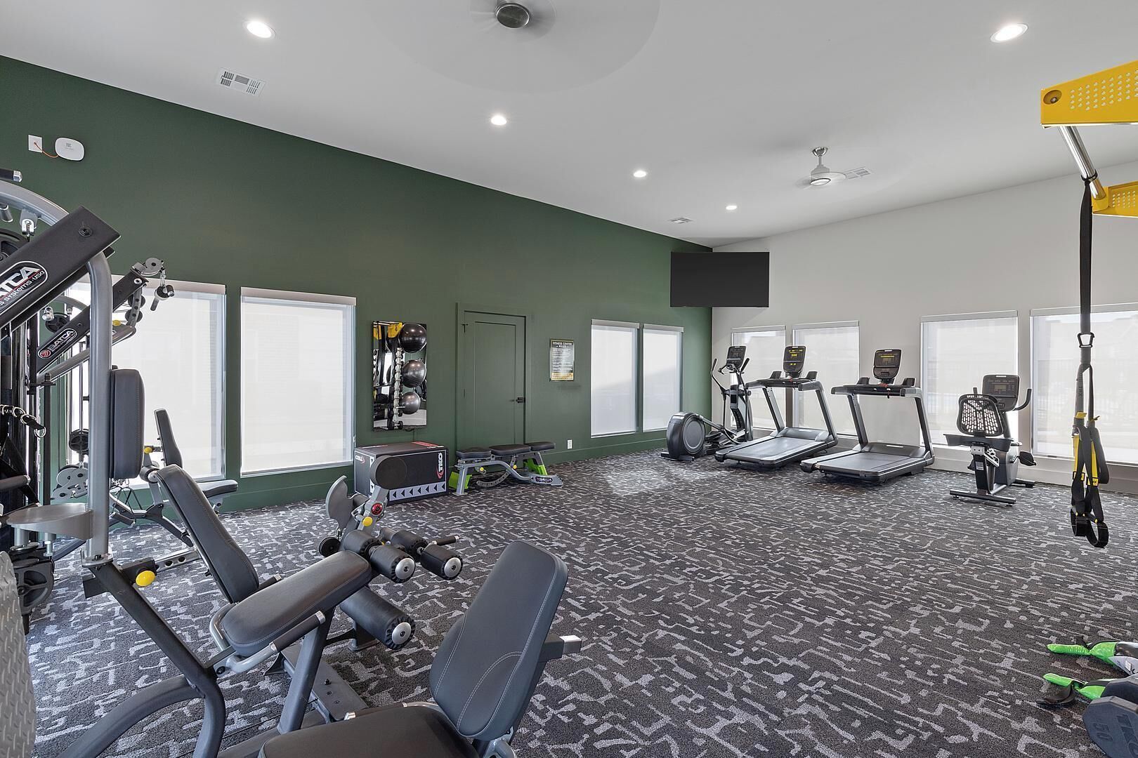 Ein Fitnessstudio mit Trainingsgeräten, Laufbändern und einem Deckenventilator.