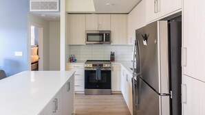 A modern kitchen with a stainless steel refrigerator, oven, and microwave, light wood cabinets, and a white countertop. - Landing | Chic 1BD, Game Room, Gym (Murrieta)