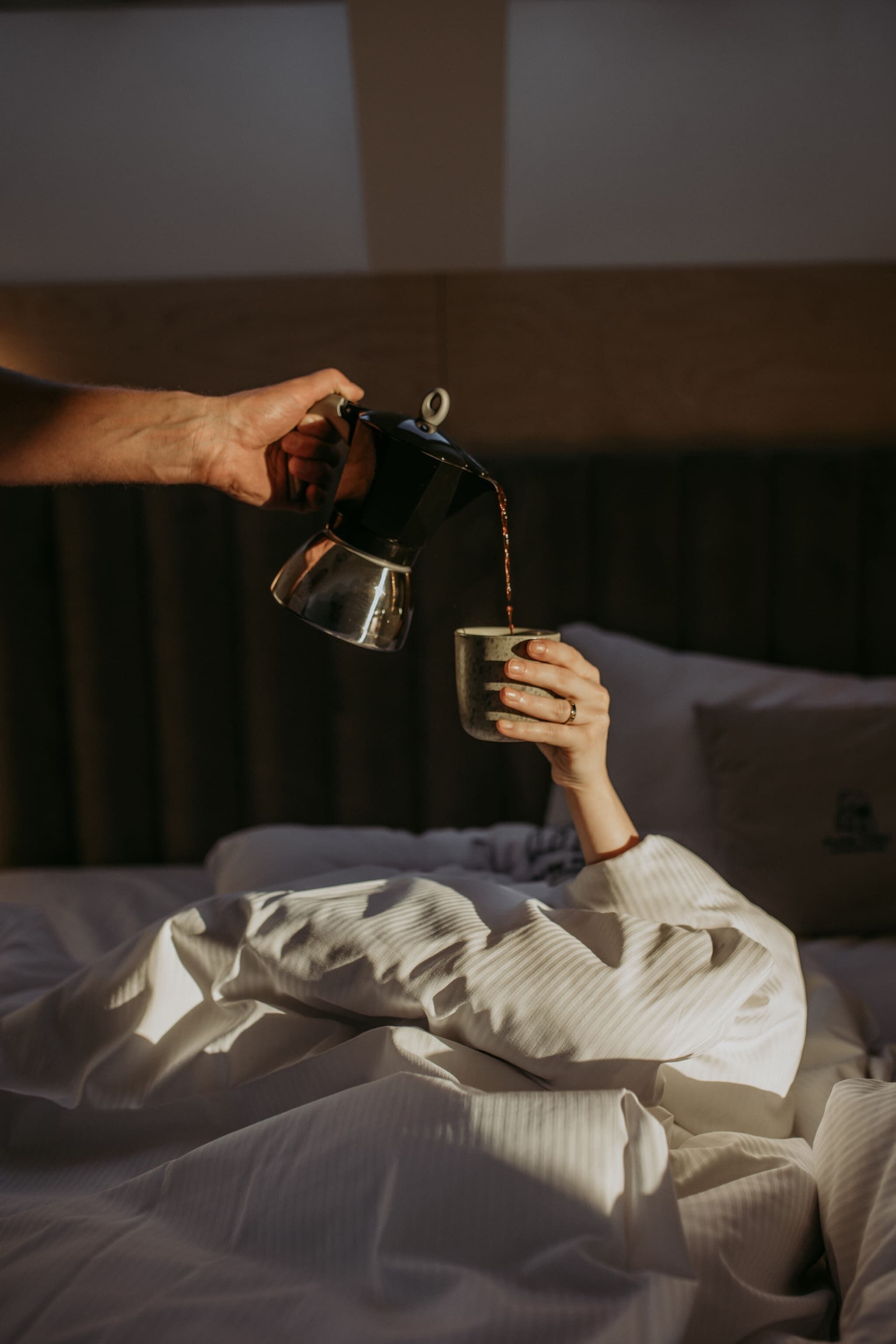 A person pouring a drink into a cup on a bed.