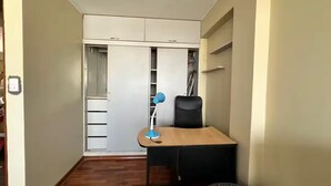 Una stanza compatta con una scrivania in legno, una sedia, un armadio e mensole.