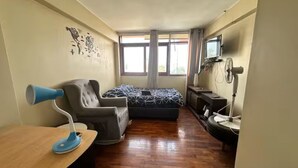 Una stanza con un letto, una scrivania, una sedia, una TV e una finestra.