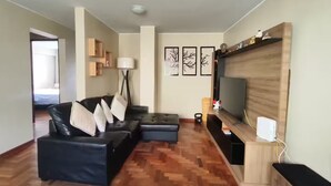 Un soggiorno moderno con un divano componibile, una TV a schermo piatto montata su una parete in legno, una lampada da terra e un pavimento in parquet a spina di pesce.