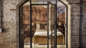 A room with a bed, a nightstand, a lamp, and a view through an arched doorway. - Historic Diplomat Suite w/Parking - The Harmony (Philadelphia)